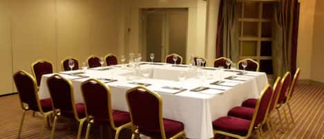 A conference room with a round table, red chairs, and white tablecloths.