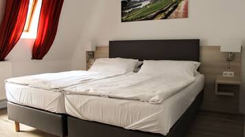 Uma cama de casal com lençóis brancos, cabeceira escura, duas mesas de cabeceira com abajures e um quadro com paisagem na parede.
