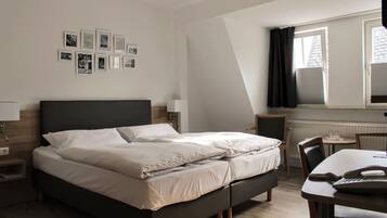 A neatly arranged bedroom with a bed, bedside tables, a desk, and chairs.