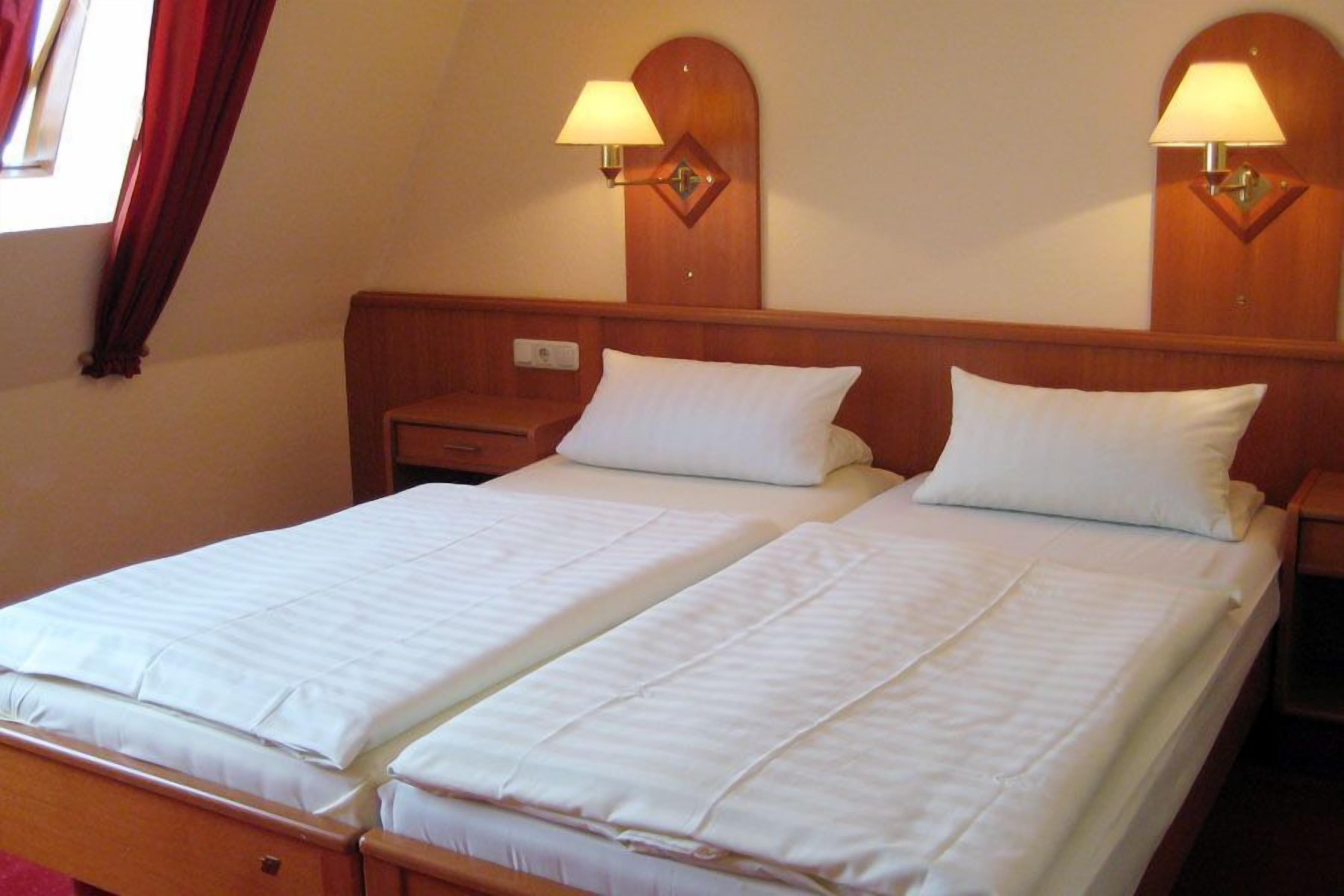A double bed with white linens, two bedside tables, and two wall-mounted lamps.