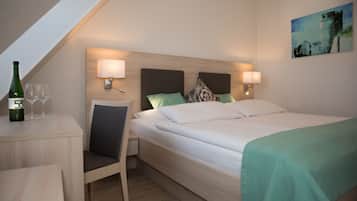 Habitación de hotel con cama, lámparas de noche, escritorio con botella y vasos, y un cuadro en la pared.