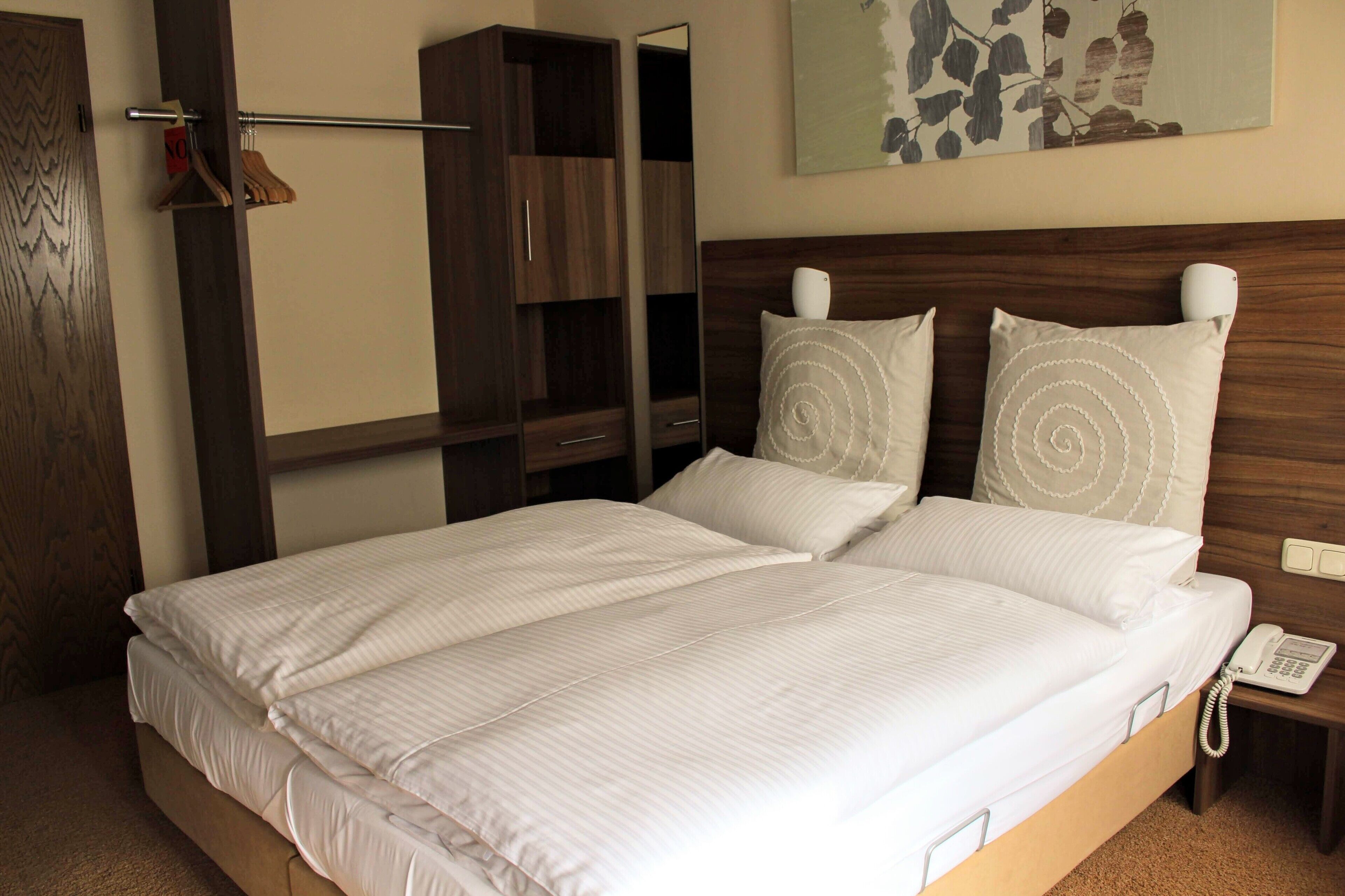 Una cama bien hecha con sábanas blancas, cabecera de madera y teléfono en la mesita de noche.