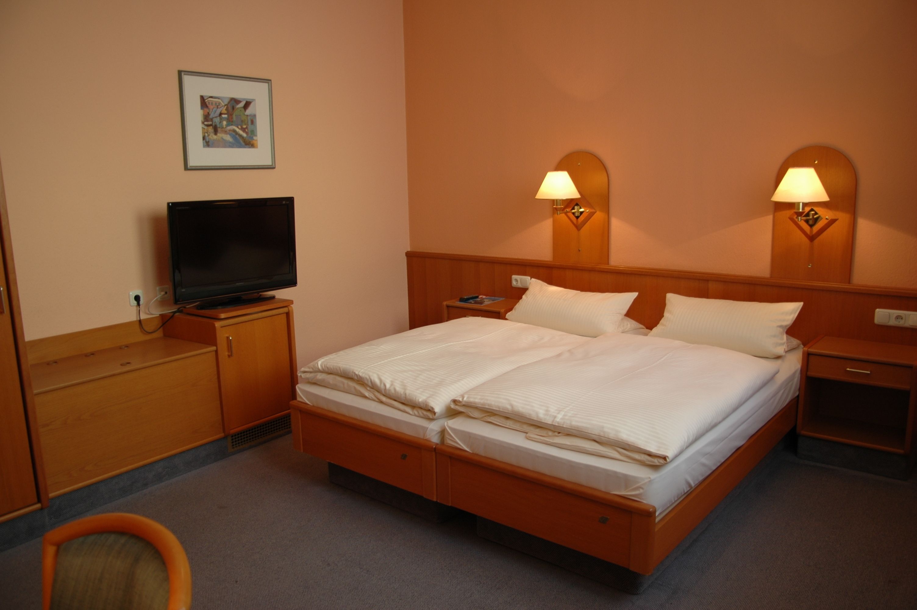 Una habitación de hotel con una cama, televisión, escritorio y dos lámparas de noche.