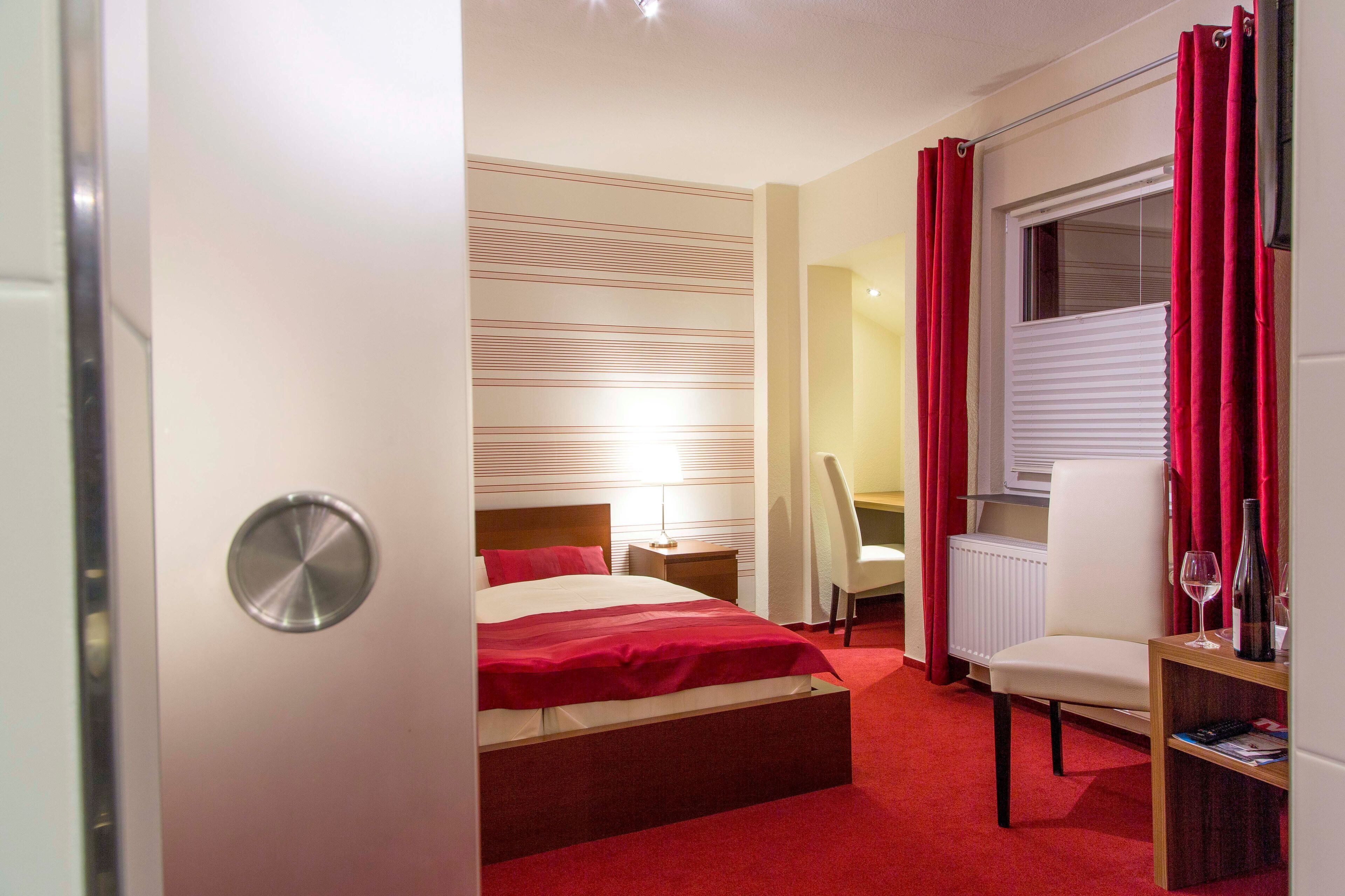 A hotel room with a bed, a desk, a chair, a radiator, and a window with curtains.