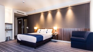 A hotel room with a large bed, bedside lamps, a chair, and a wall-mounted heater. - Holiday Inn Express Wakefield by IHG (Wakefield)
