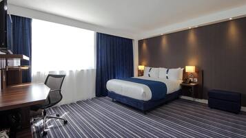 Quarto de hotel com cama, mesas de cabeceira, escrivaninha e cadeira.