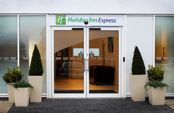 A Holiday Inn Express with a glass door entrance, two potted plants, and a visible car inside.