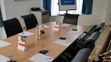 A conference room with a long table, black chairs, a projector screen, and a "Welcome" sign.