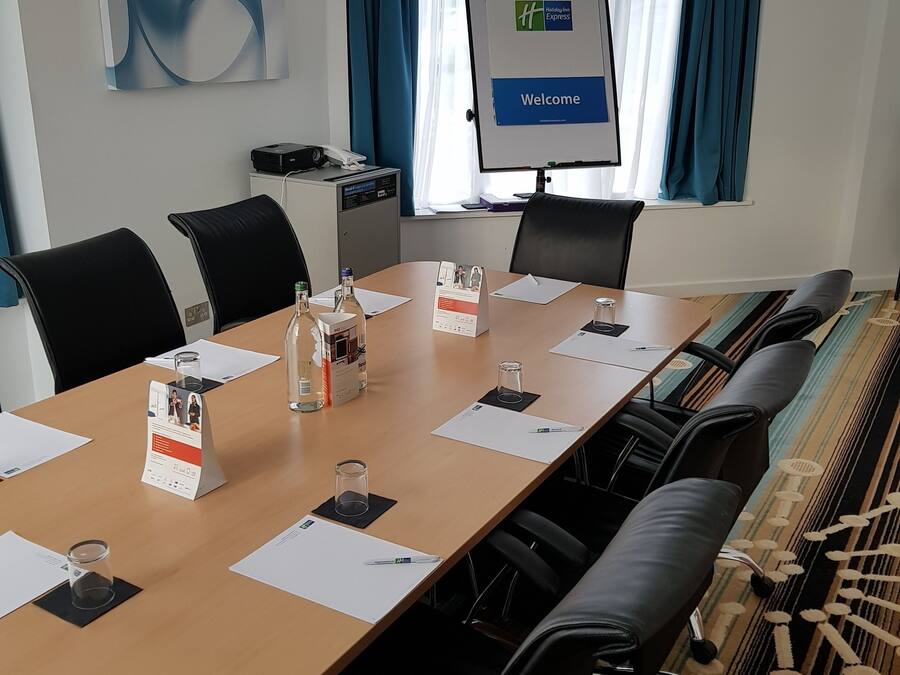 A conference room with a long table, black chairs, a projector screen, and a "Welcome" sign.