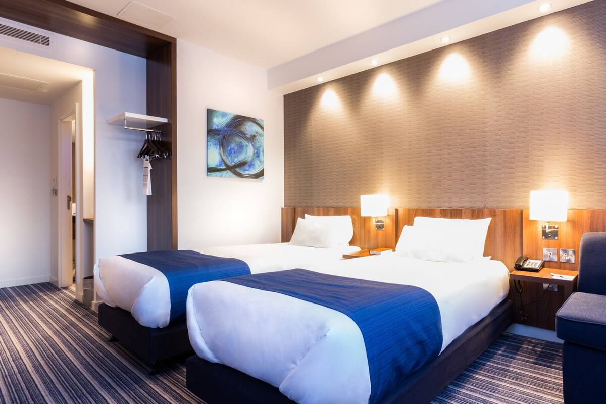 Habitación de hotel con dos camas, un escritorio, una silla, un cuadro y un teléfono en la mesita de noche.