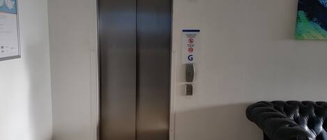 An elevator with a digital display, a fire alarm, and a sign indicating the use of the fire exit.