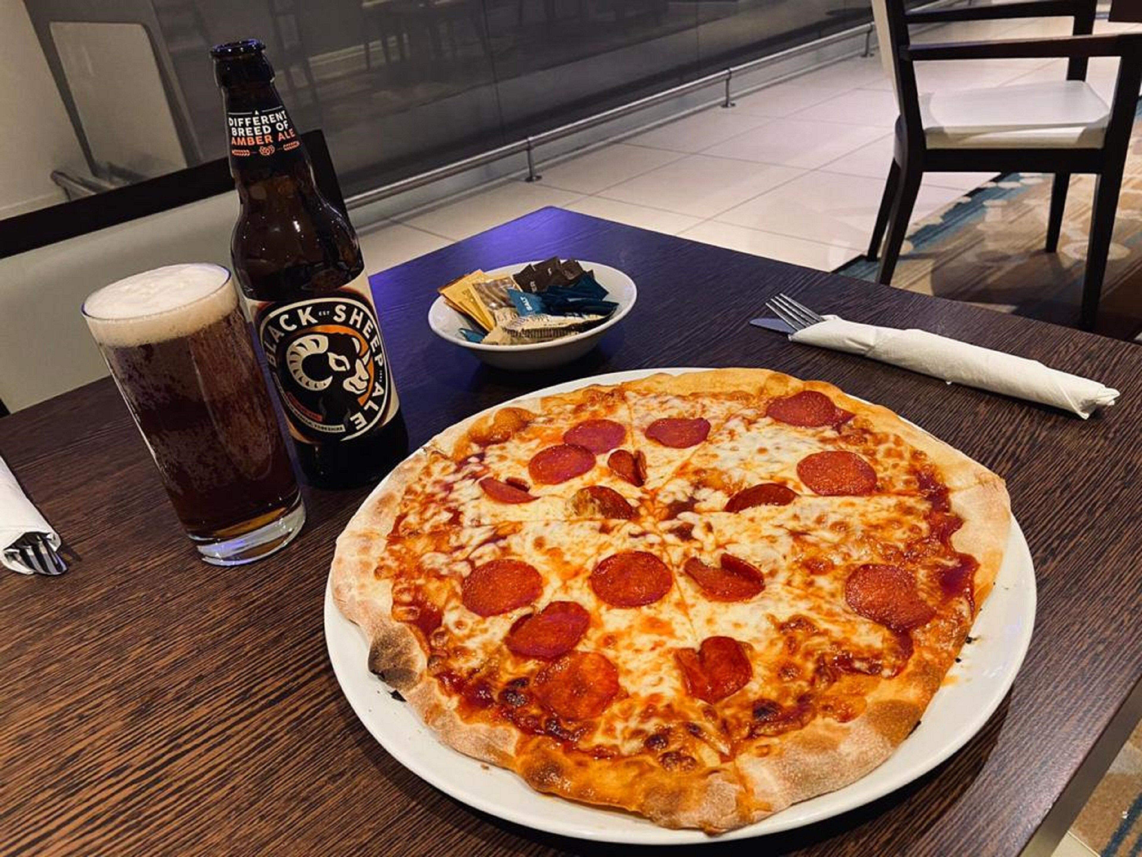 A pizza with pepperoni, a beer bottle, and a glass of beer on a table.