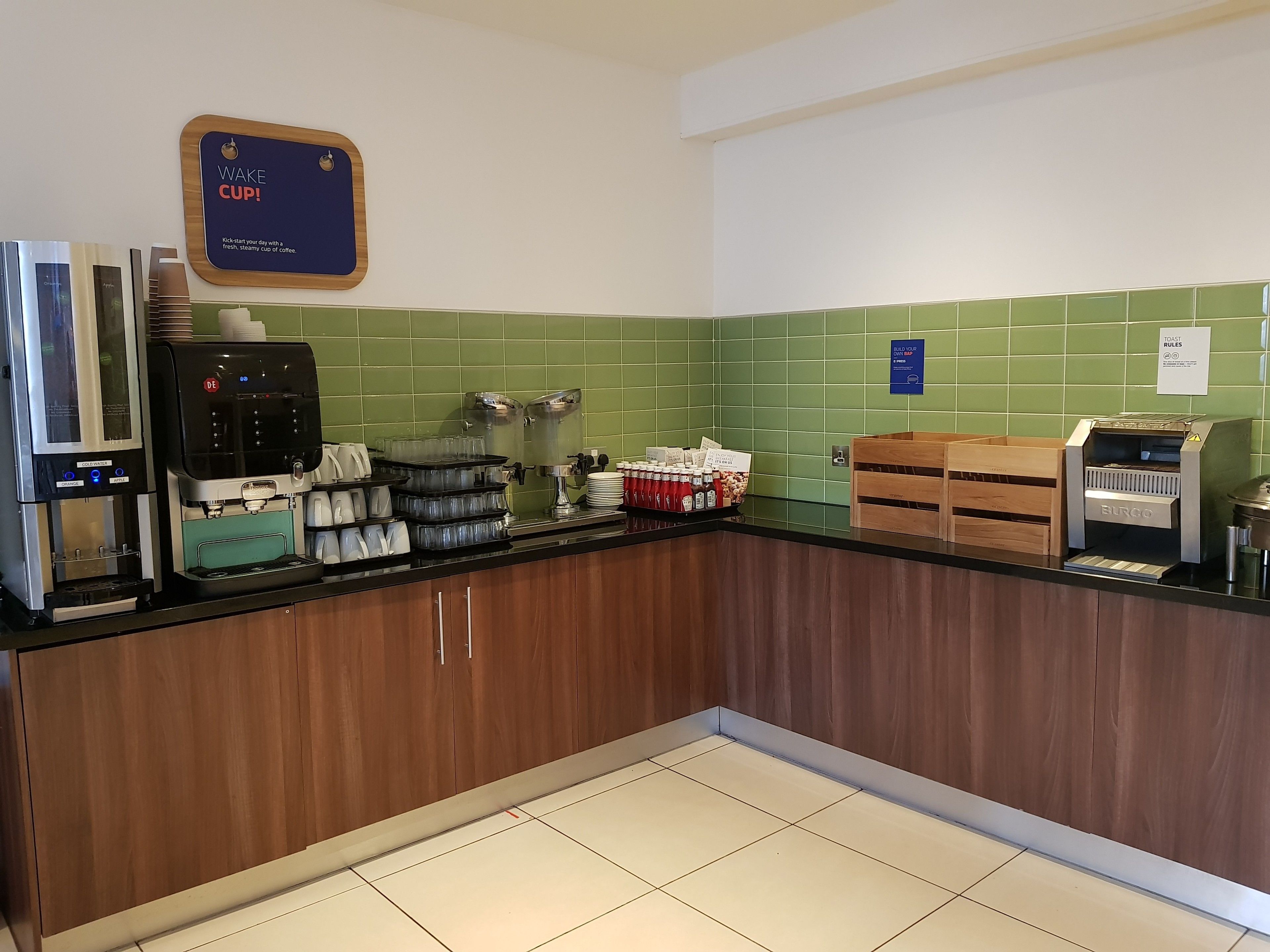 A coffee station with multiple coffee machines, a sign that reads "Wake Cup!", and a "Roast Rules" sign.