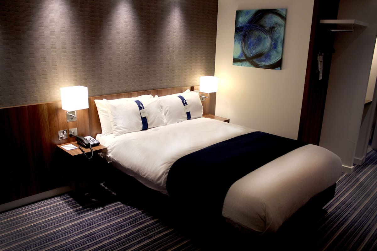 Habitación de hotel con una cama grande, dos lámparas de noche, un teléfono y un cuadro en la pared.
