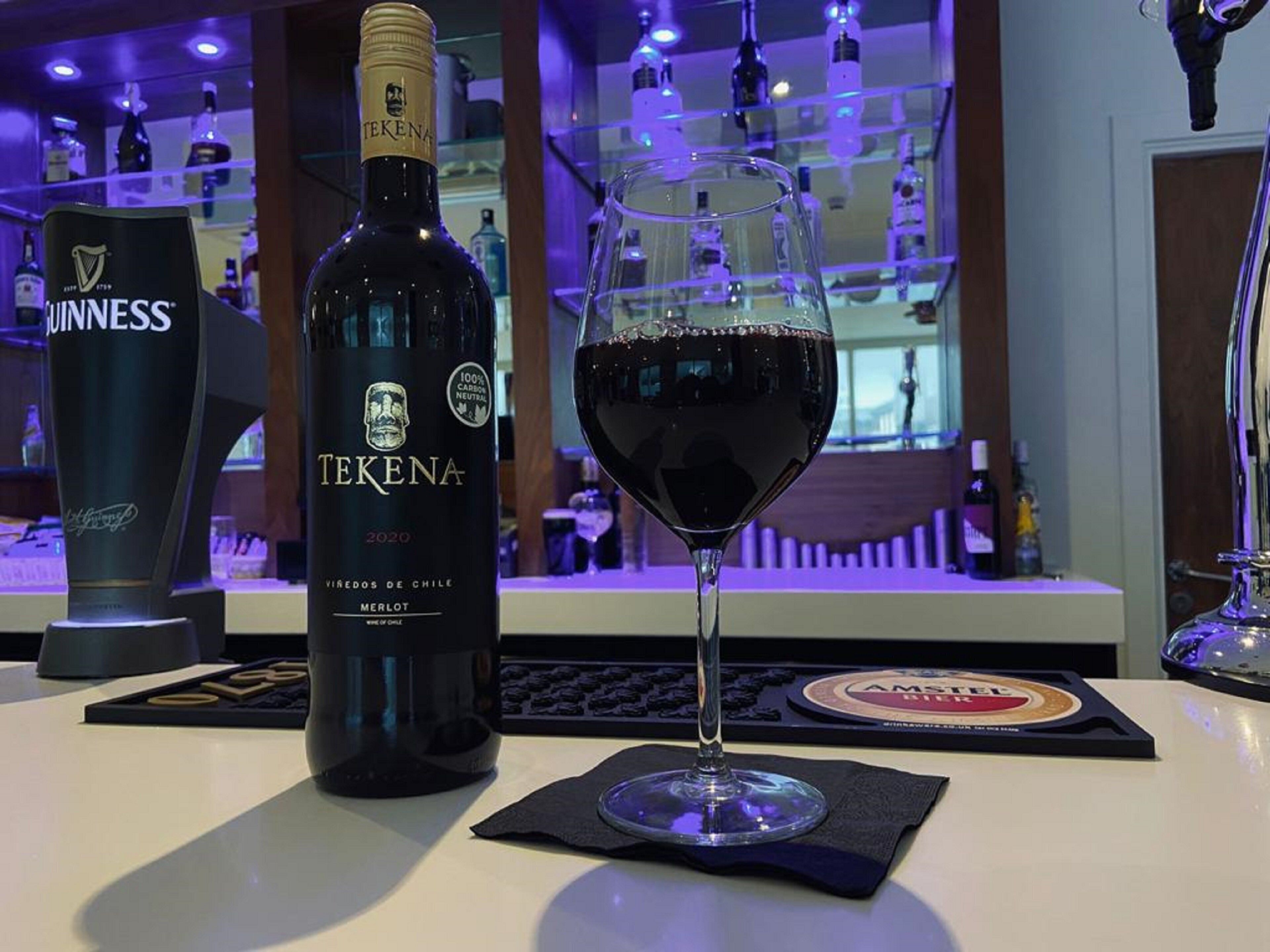 Una botella de Tekena Merlot y una copa de vino tinto sobre una barra.