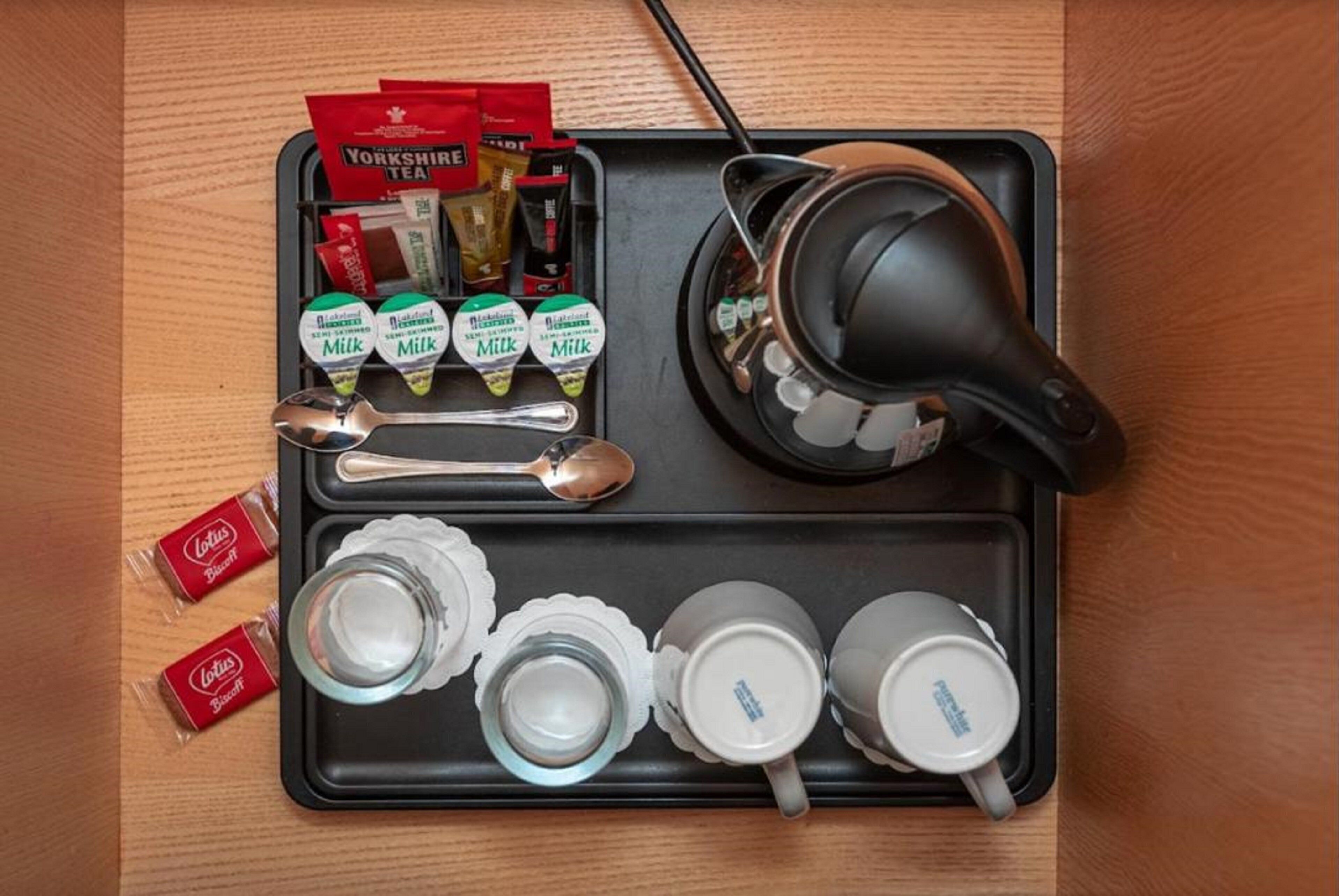 Un plateau avec des sachets de thé, des petits paquets de lait, une théière, des cuillères et des tasses.