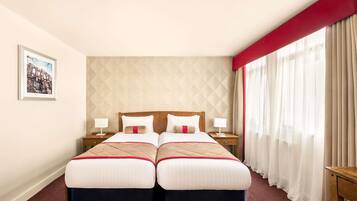 Habitación de hotel con dos camas, un ventanal con cortinas, un cuadro enmarcado en la pared y una pared de acento roja.