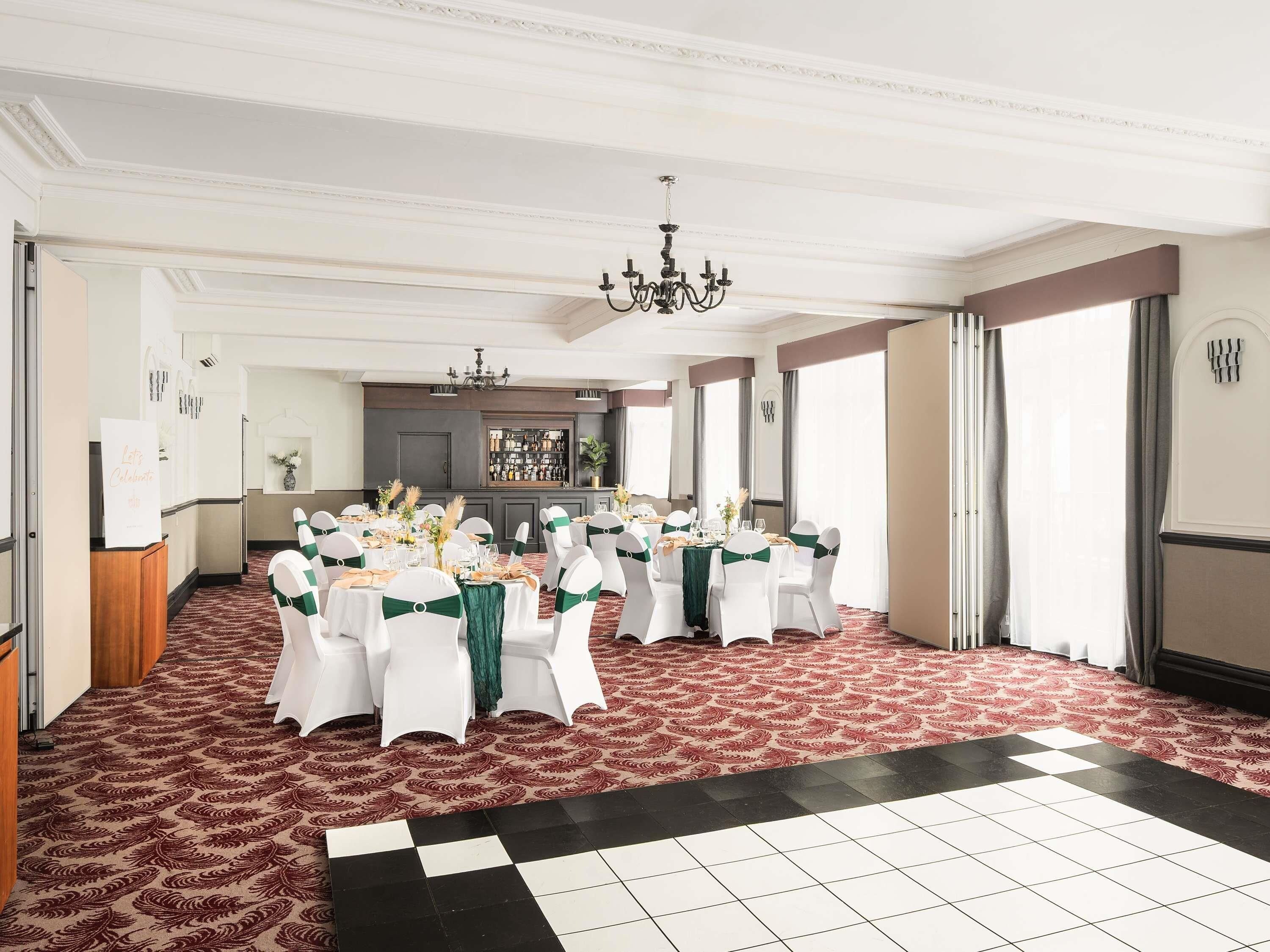 A banquet hall with round tables, white chairs, and a bar area.