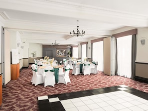 A banquet hall with round tables, white chairs, and a bar area.