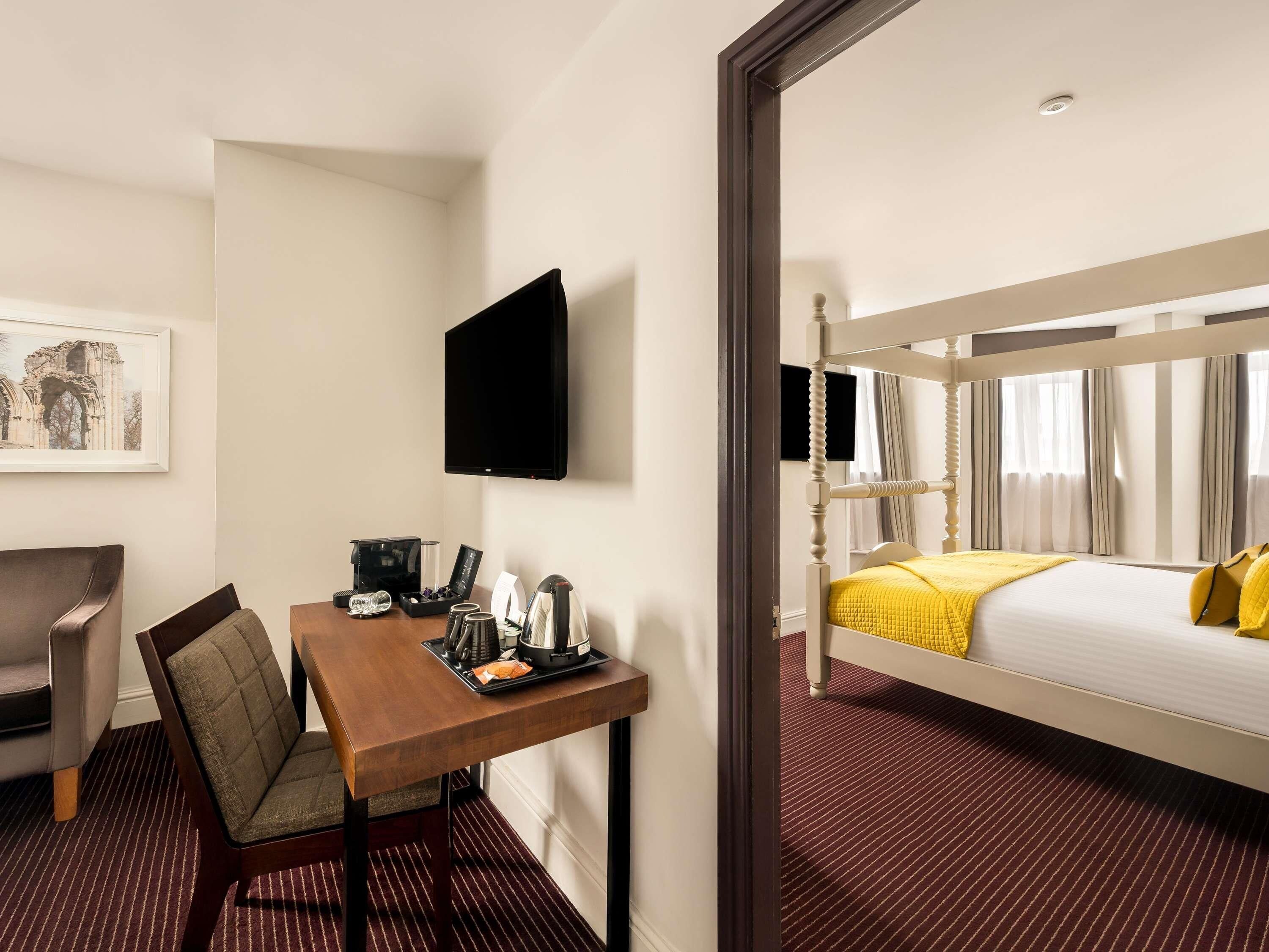 Een hotelkamer met een bed, een bureau met stoel, een televisie en een ingelijst schilderij aan de muur.