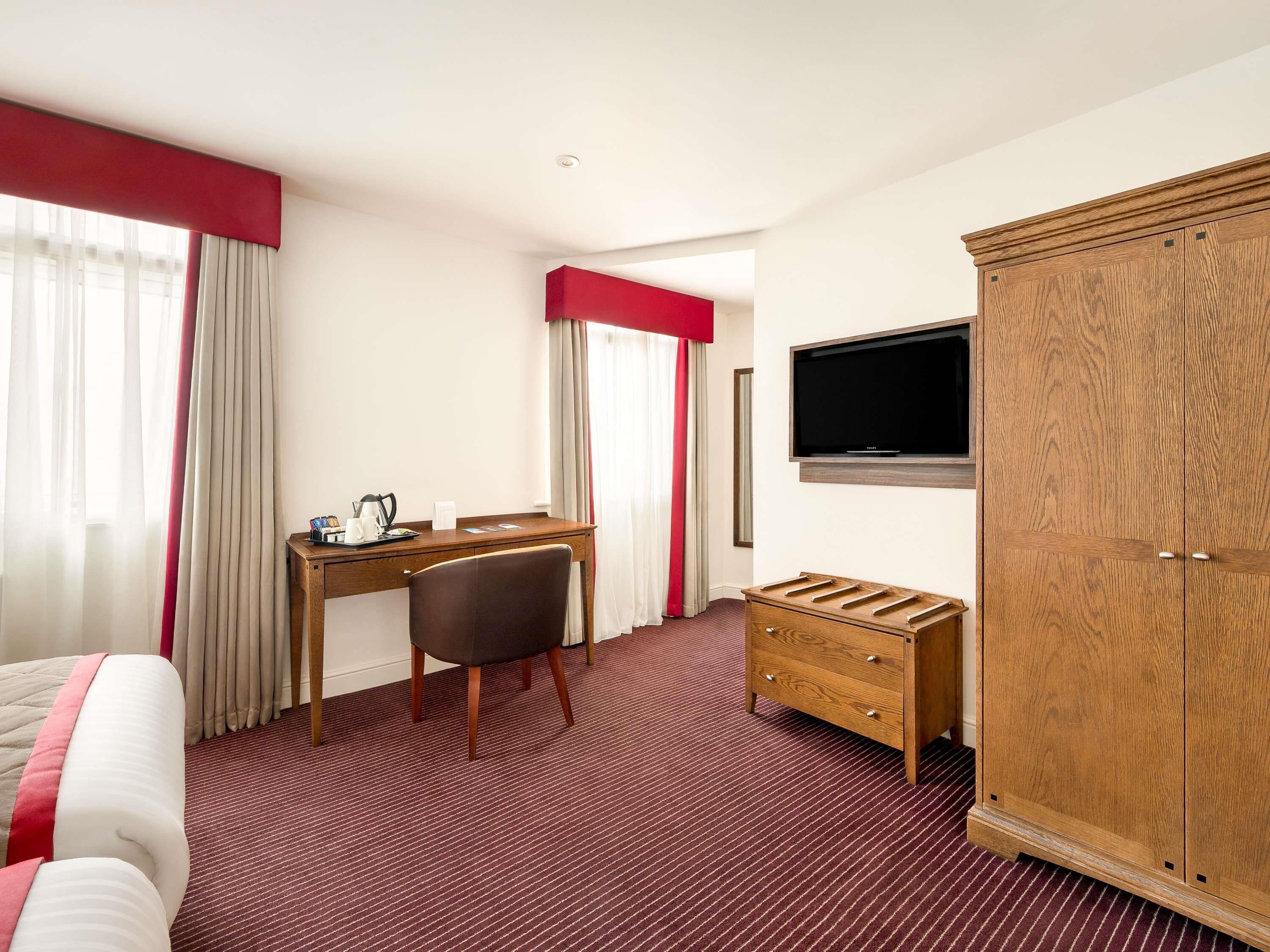 A hotel room with a bed, a desk, a chair, a TV, and a wardrobe.