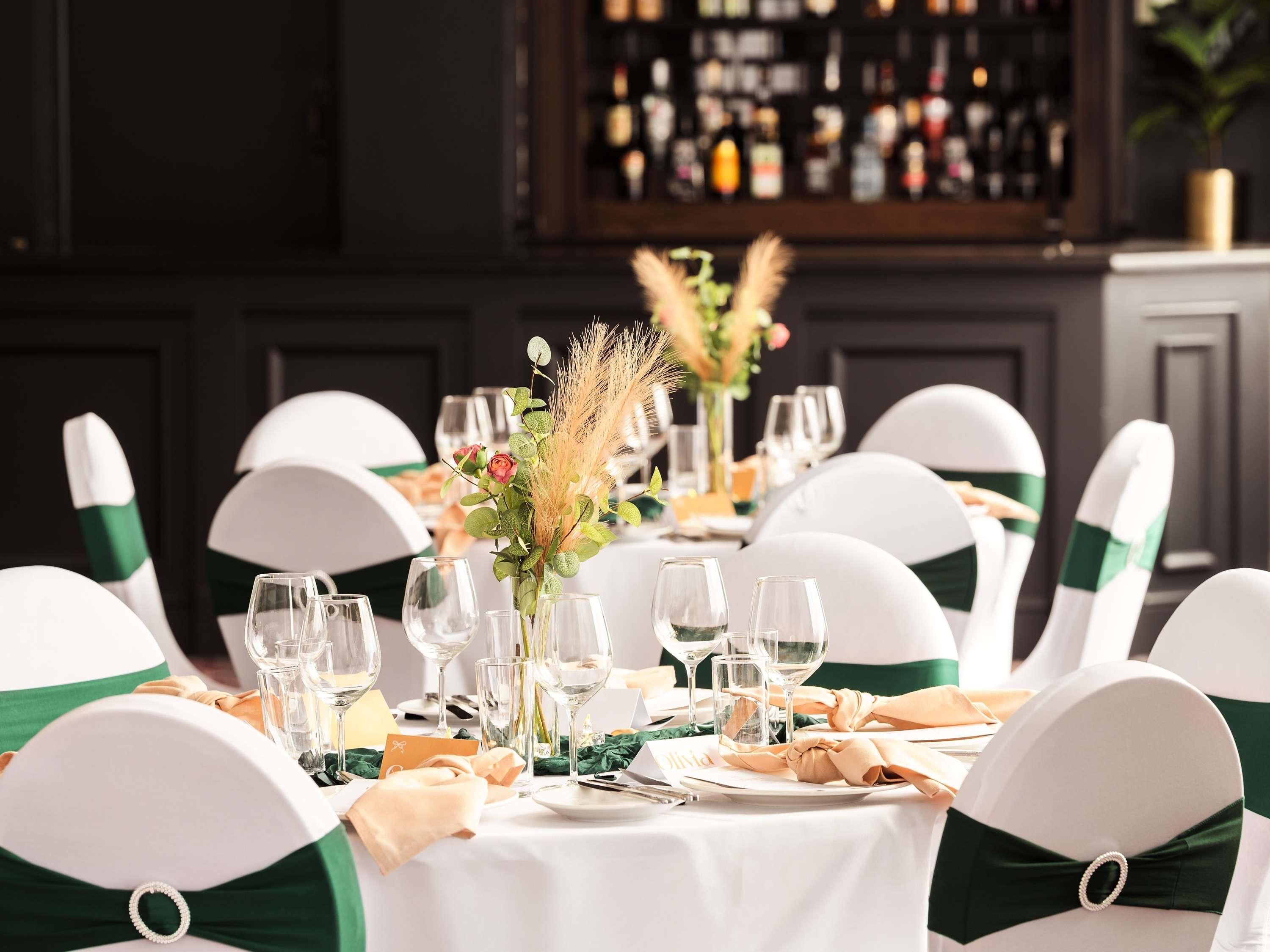 Mesa de restaurante dispuesta con sillas blancas, cintas verdes y un mantel blanco.