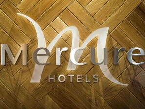 Ein Logo mit dem Schriftzug "Mercure" und "HOTELS" auf einem Holzboden mit Fischgrätmuster.
