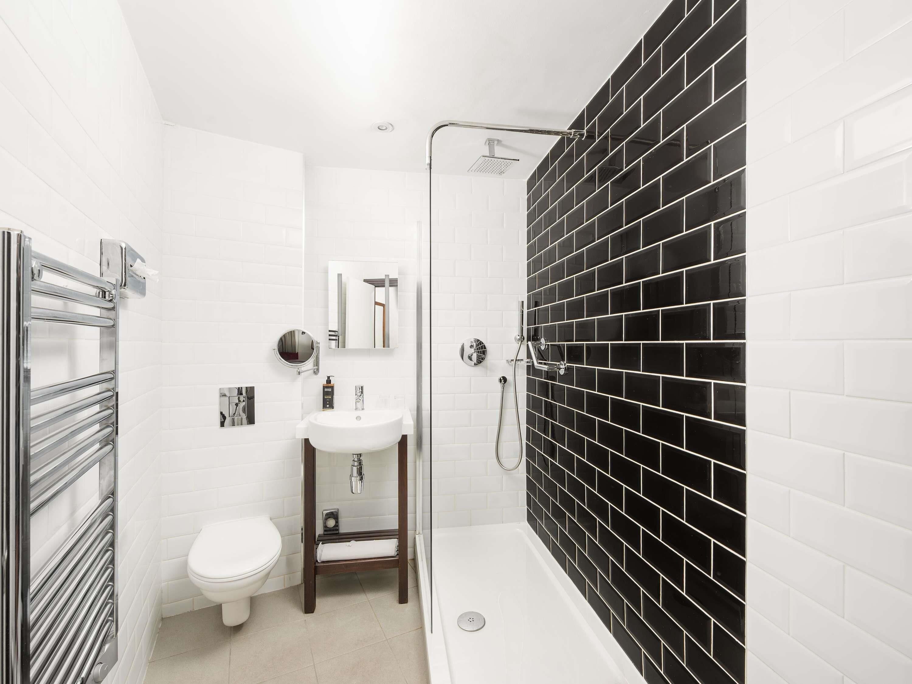 Un baño moderno con inodoro blanco, lavamanos, espejo y zona de ducha con azulejos negros.
