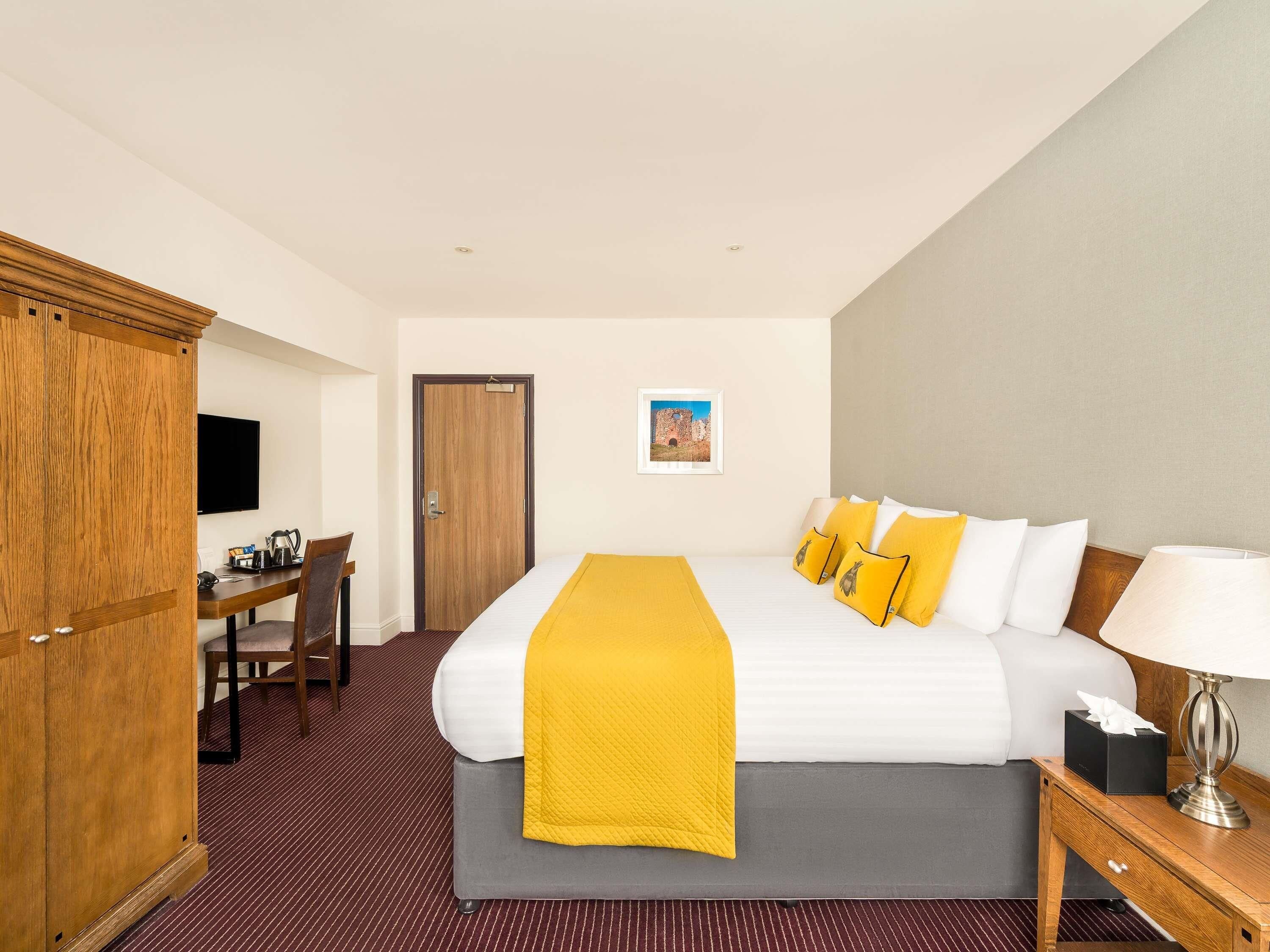 A hotel room with a bed, a desk, a chair, a wardrobe, and a television.