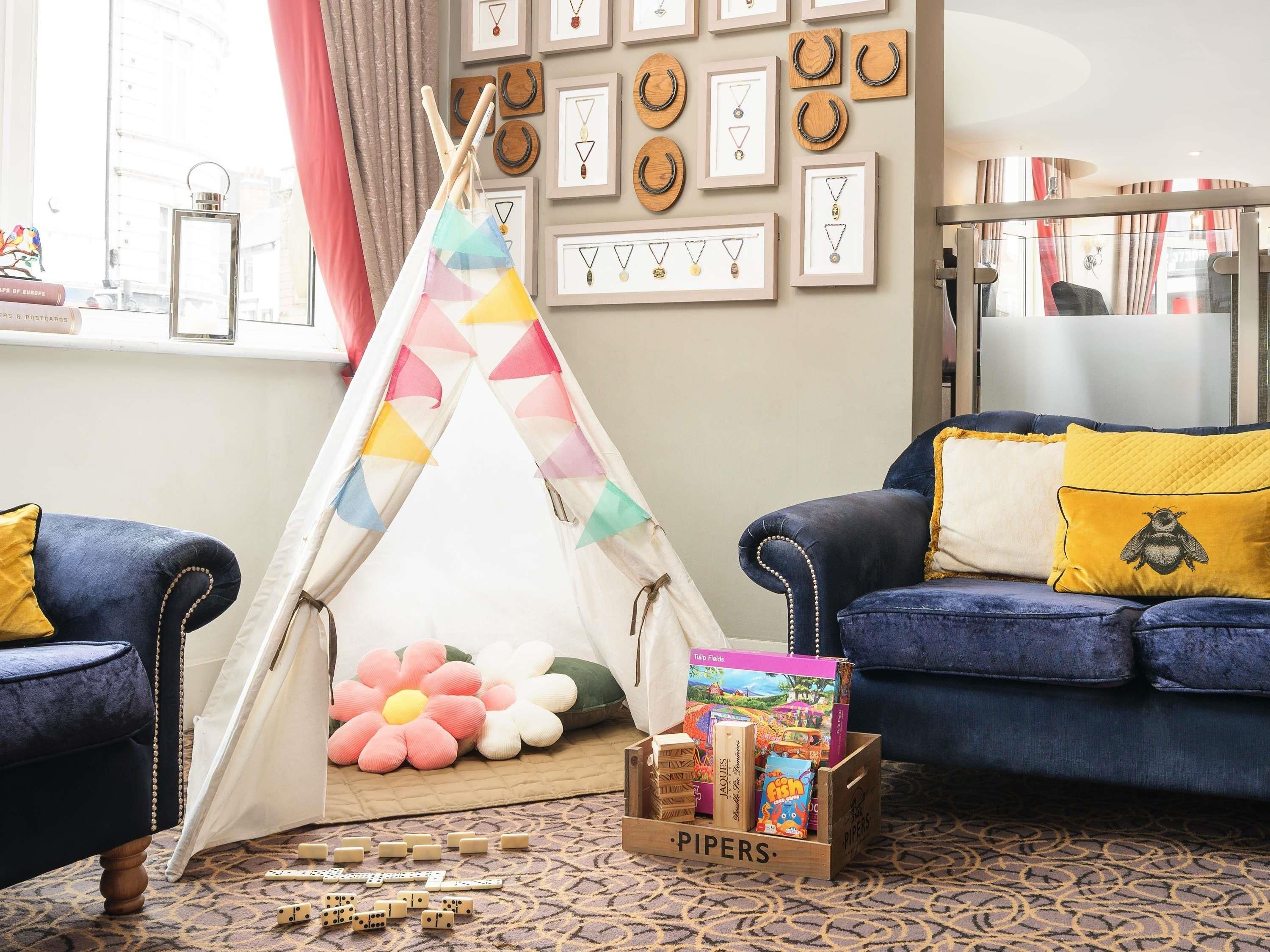 A cozy living room with a blue sofa, a colorful teepee, and a box of Pipers dice.