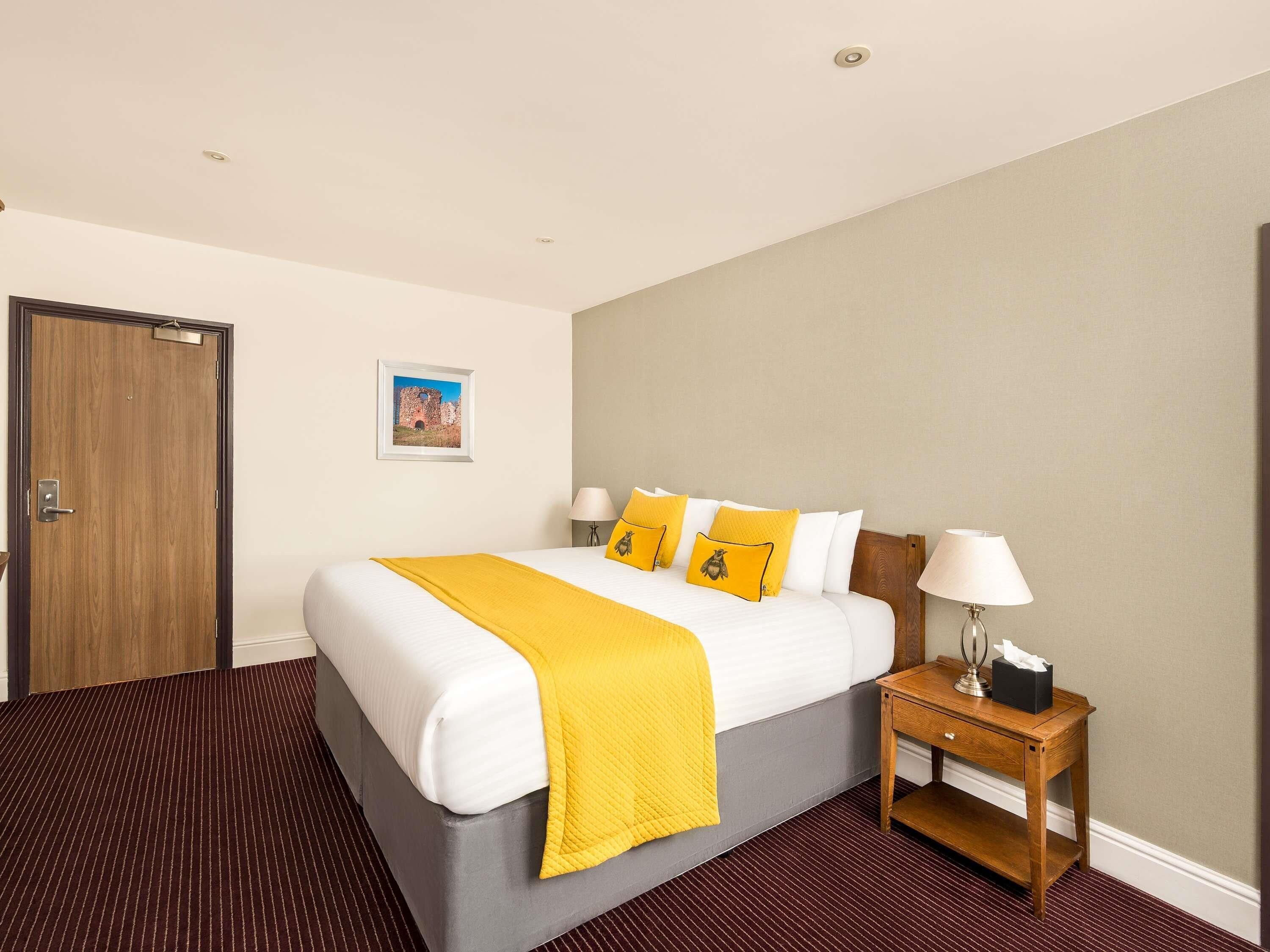 A hotel room with a large bed, a wooden nightstand, a lamp, and a picture on the wall.