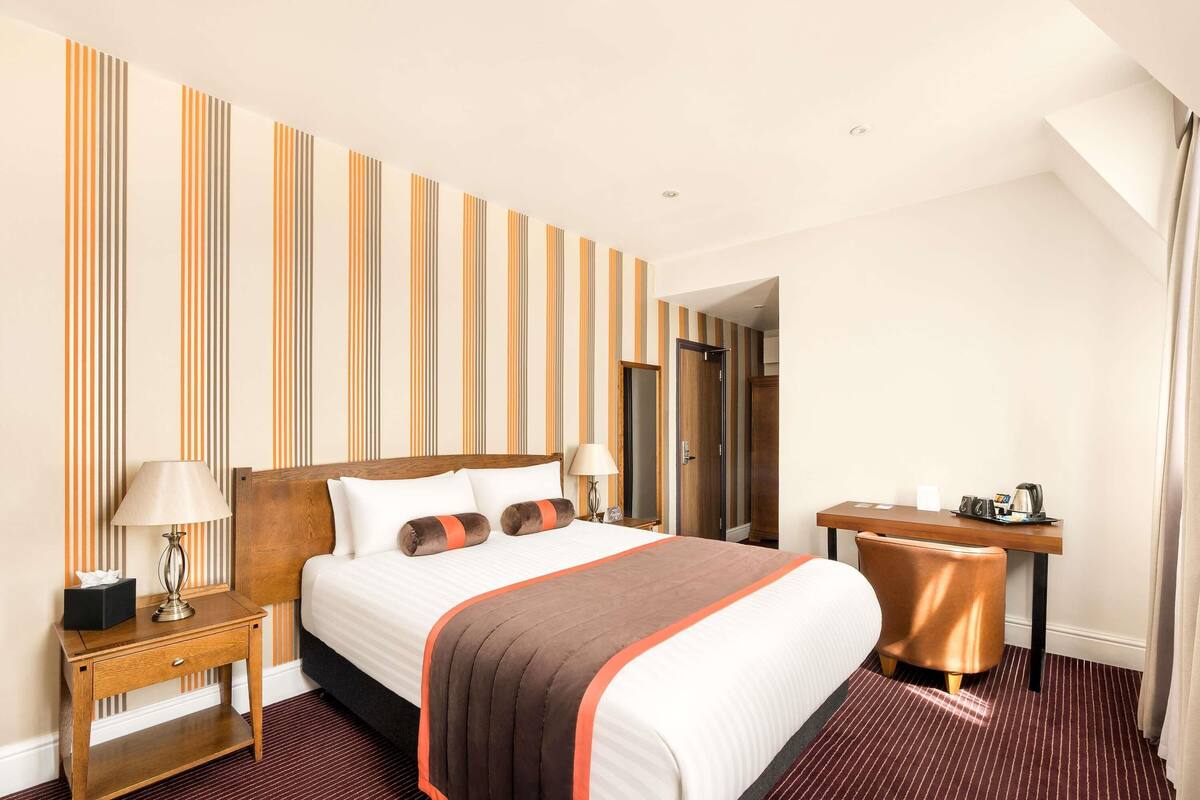 Een hotelkamer met een bed, nachtkastjes, een bureau en een spiegel.