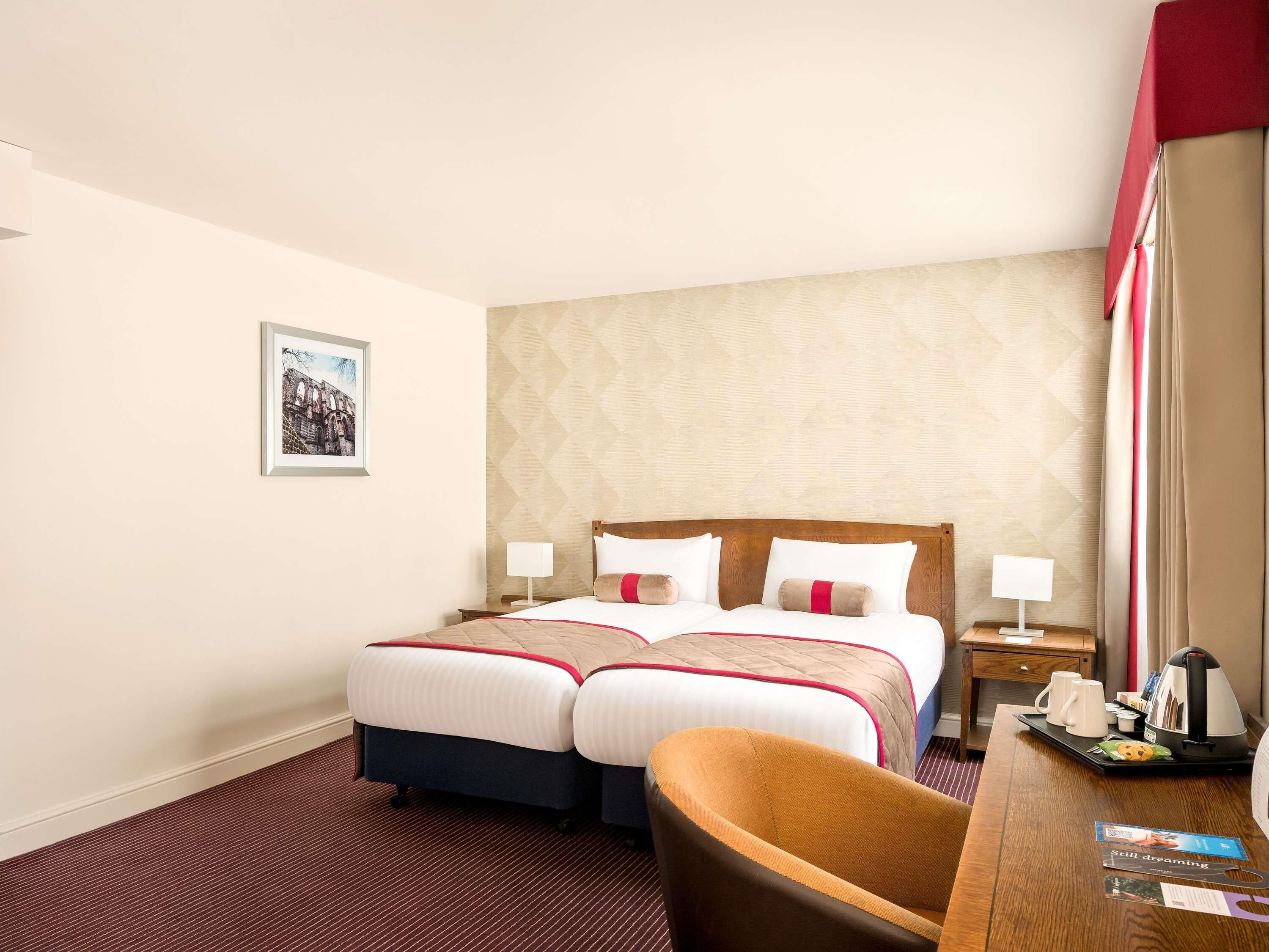 Habitación de hotel con cama doble, dos mesitas de noche, un escritorio con silla y un cuadro en la pared.