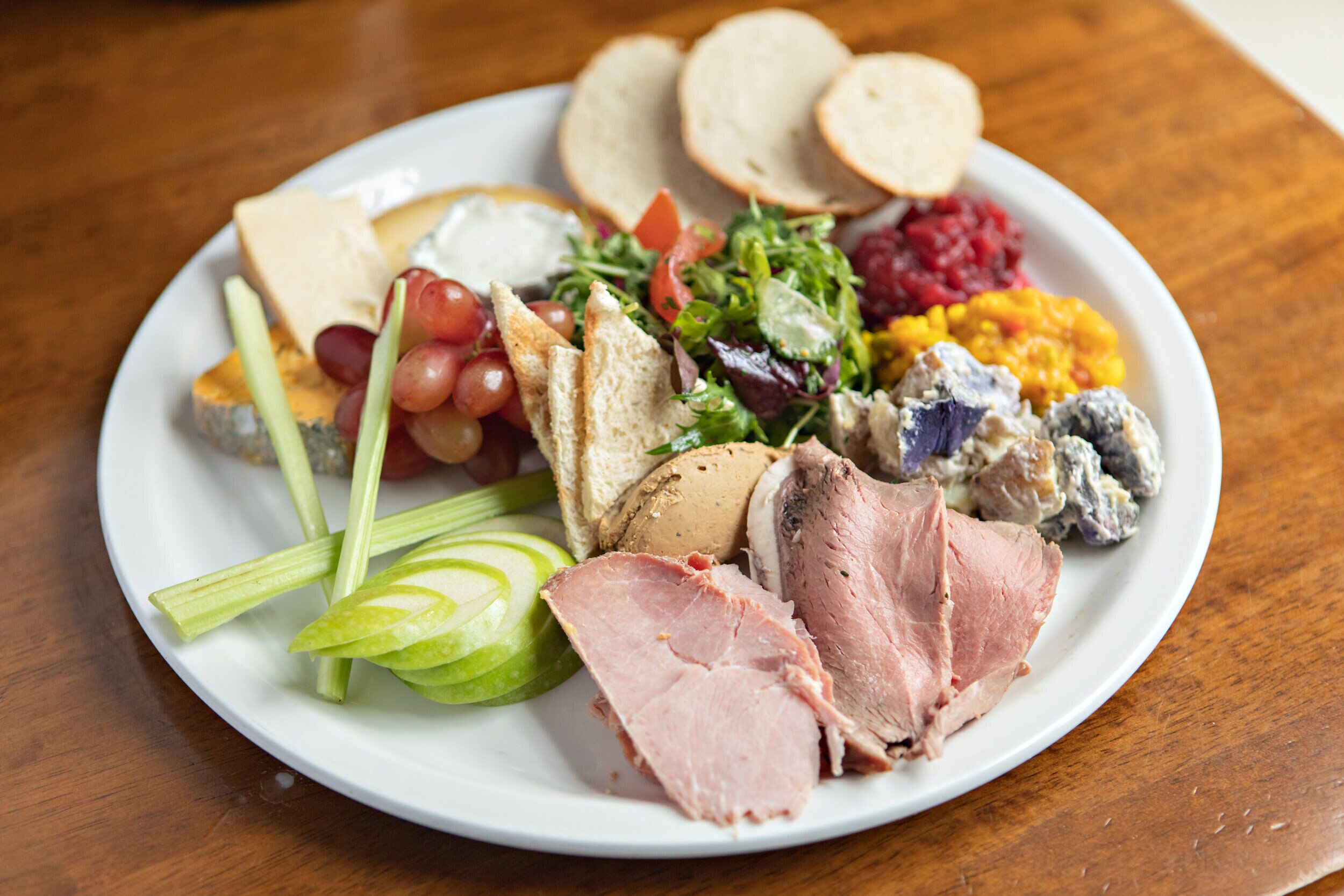 Un plato con una variedad de alimentos, entre ellos jamón en rodajas, queso, uvas y diferentes ensaladas.