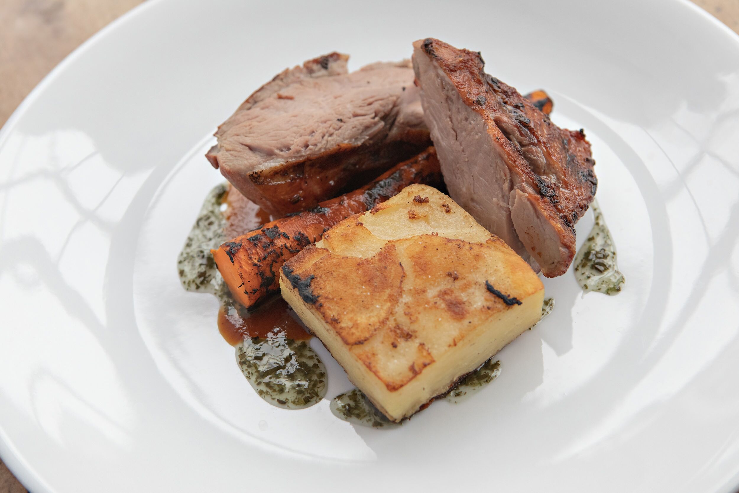 A plate with slices of roasted meat and a piece of roasted potato.
