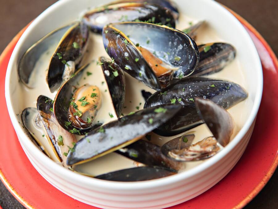 Eine Schüssel mit Muscheln in cremiger Soße, garniert mit Kräutern.