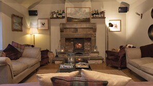 A cozy living room with a stone fireplace, comfortable sofas, and a coffee table with magazines. - The White Swan Inn (Pickering)