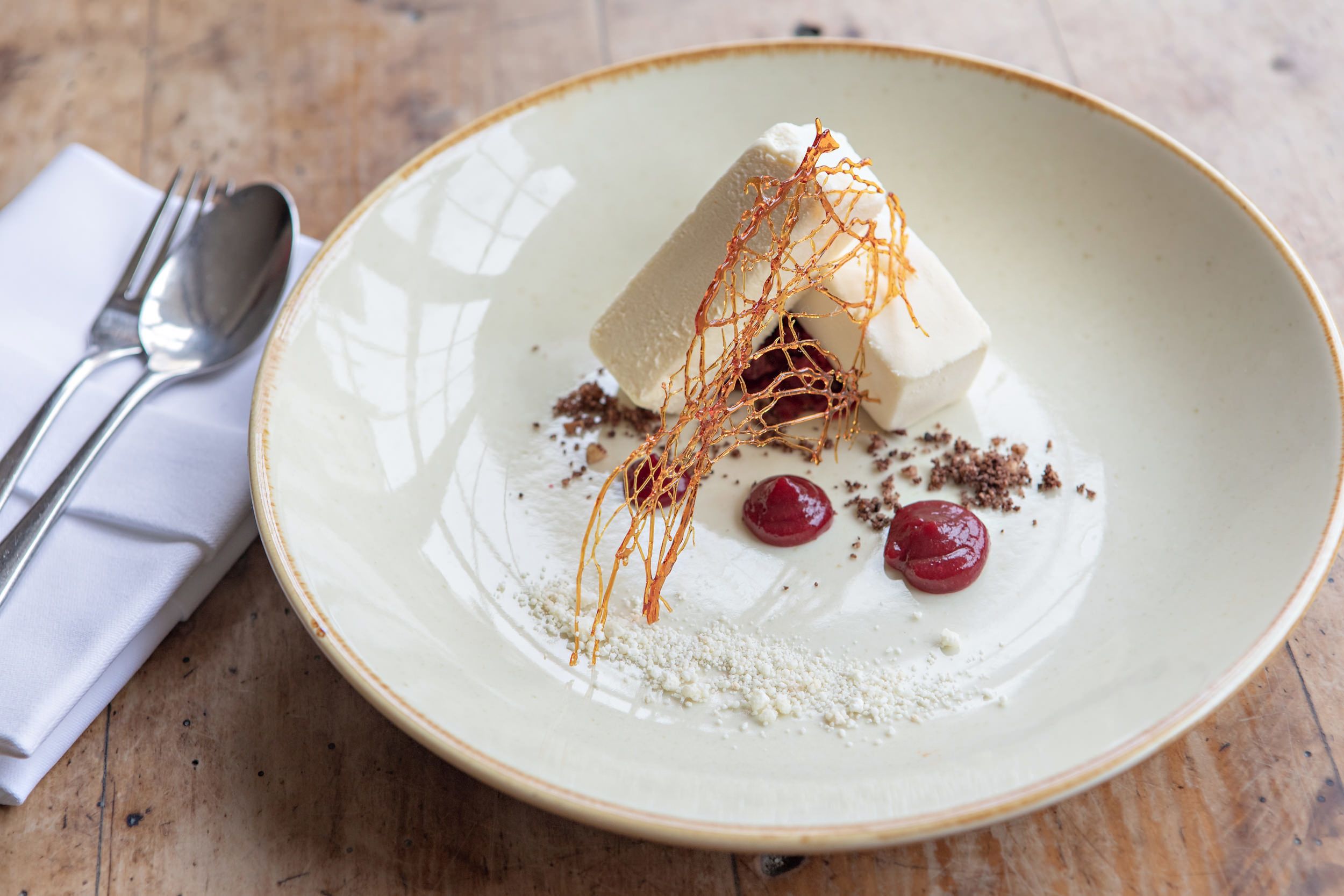A dessert on a ceramic plate with a fork and spoon beside it.