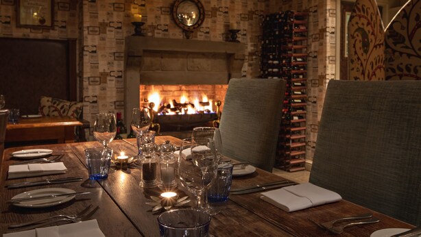 A dining table set for a meal with a fireplace in the background. - The White Swan Inn (Pickering)