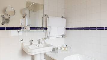 A bathroom with a white sink, a mirror, a glass shelf with toiletries, and a towel rack.