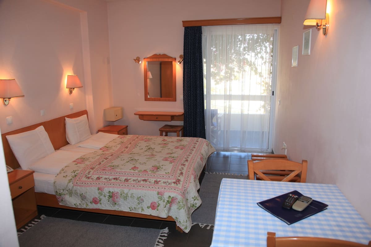 Une chambre d’hôtel comprenant un lit, des tables de chevet, un bureau avec une chaise, un miroir et une fenêtre avec des rideaux.