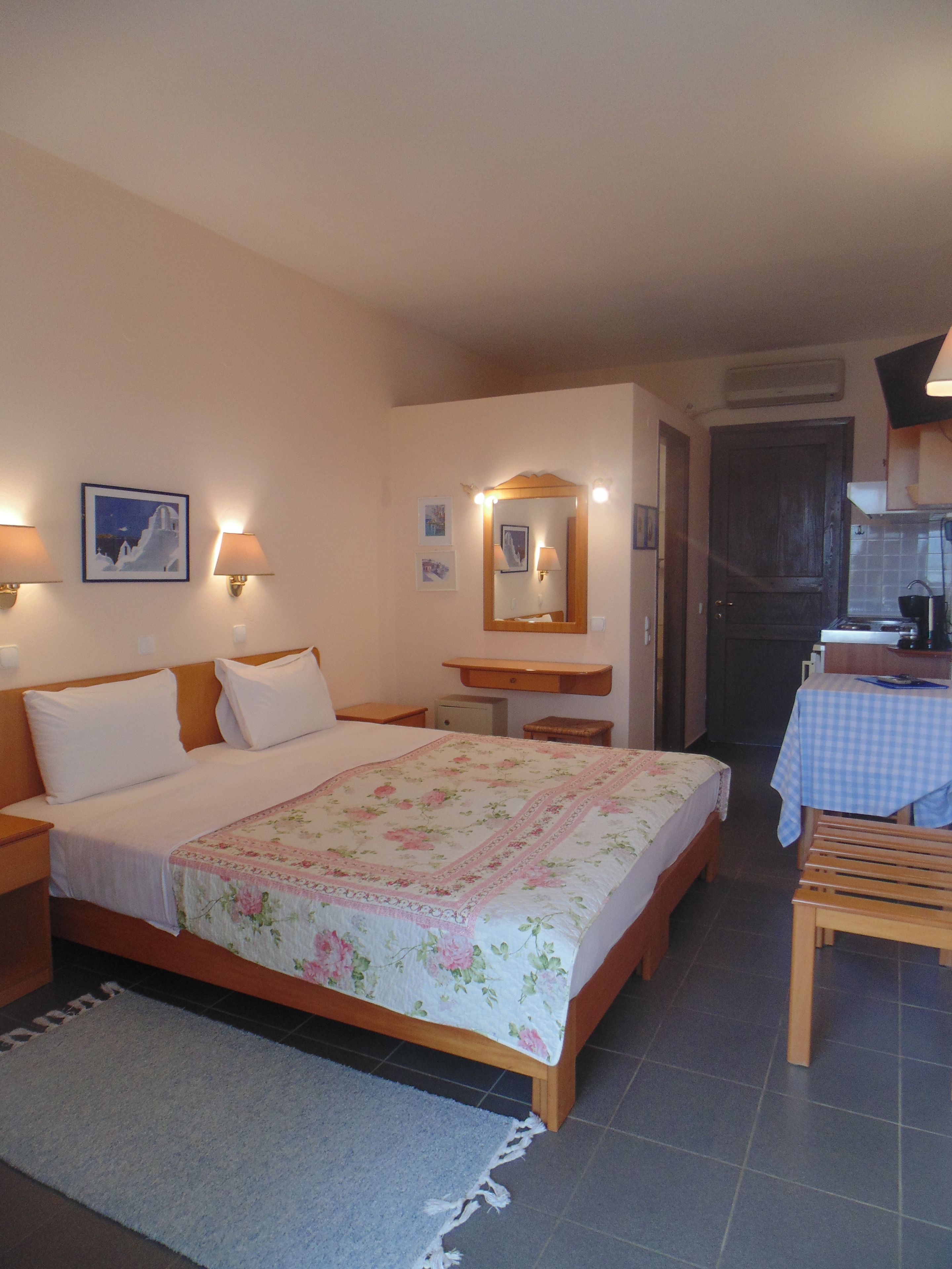 A bedroom with a bed, bedside tables, a mirror, and a small kitchenette.