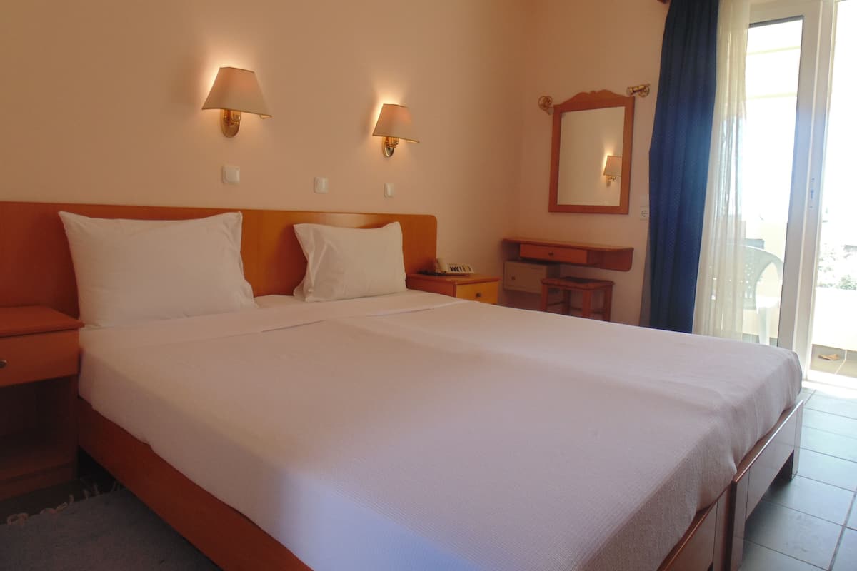 Une chambre d’hôtel avec un grand lit, deux lampes de chevet, un petit bureau, un miroir et une porte-fenêtre coulissante donnant sur l’extérieur.