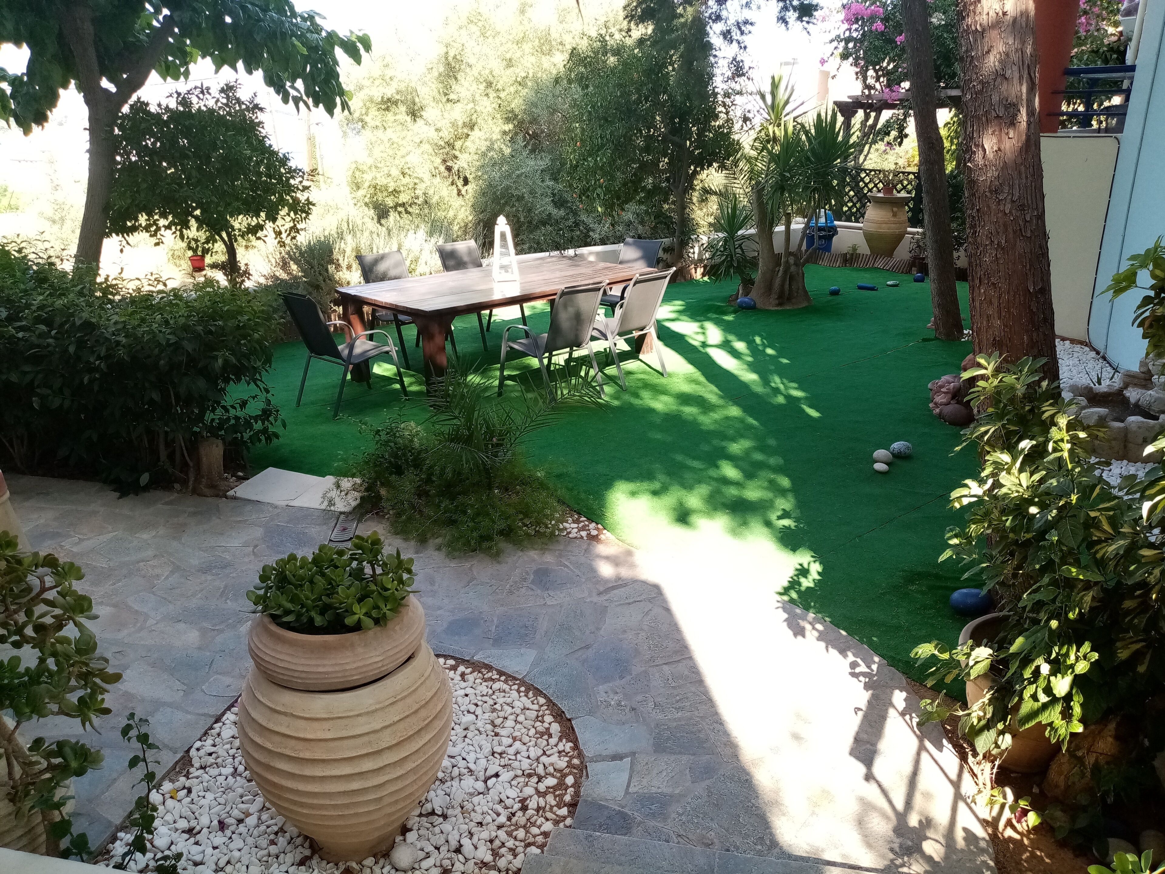 A patio with a wooden table and chairs, surrounded by greenery and a small garden area.