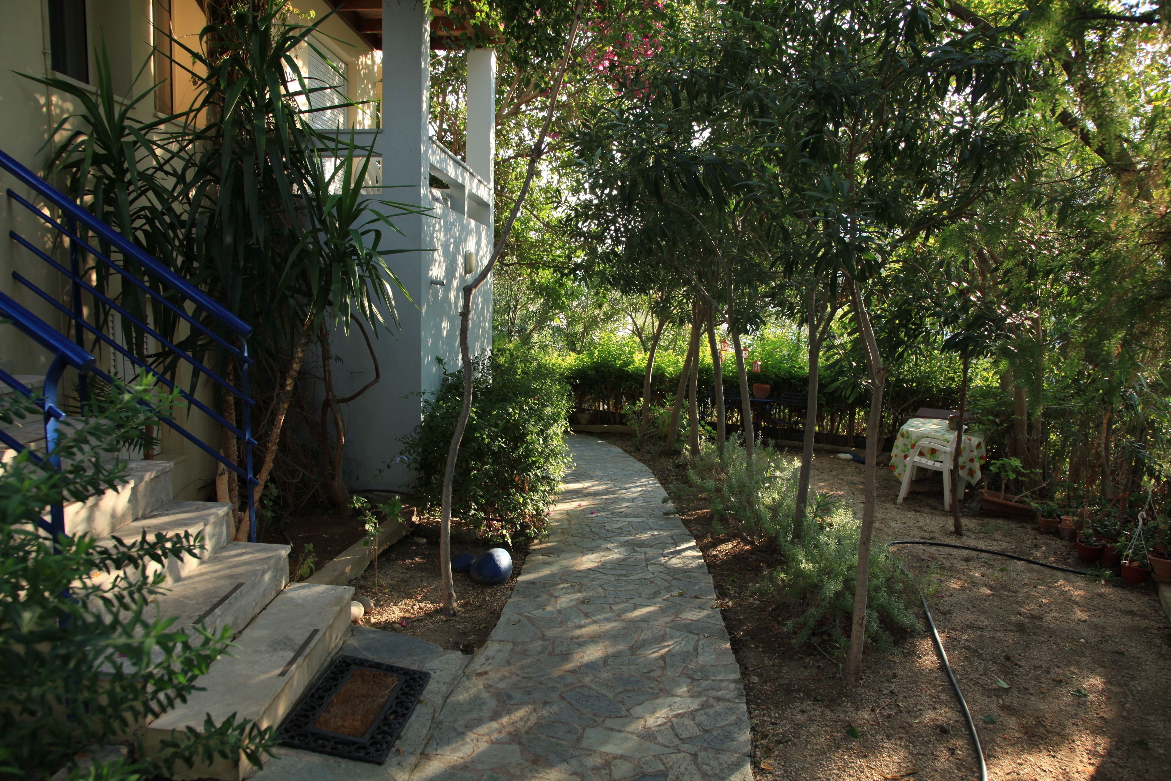 A stone pathway leading to a house with a blue railing and a small table with a cloth.
