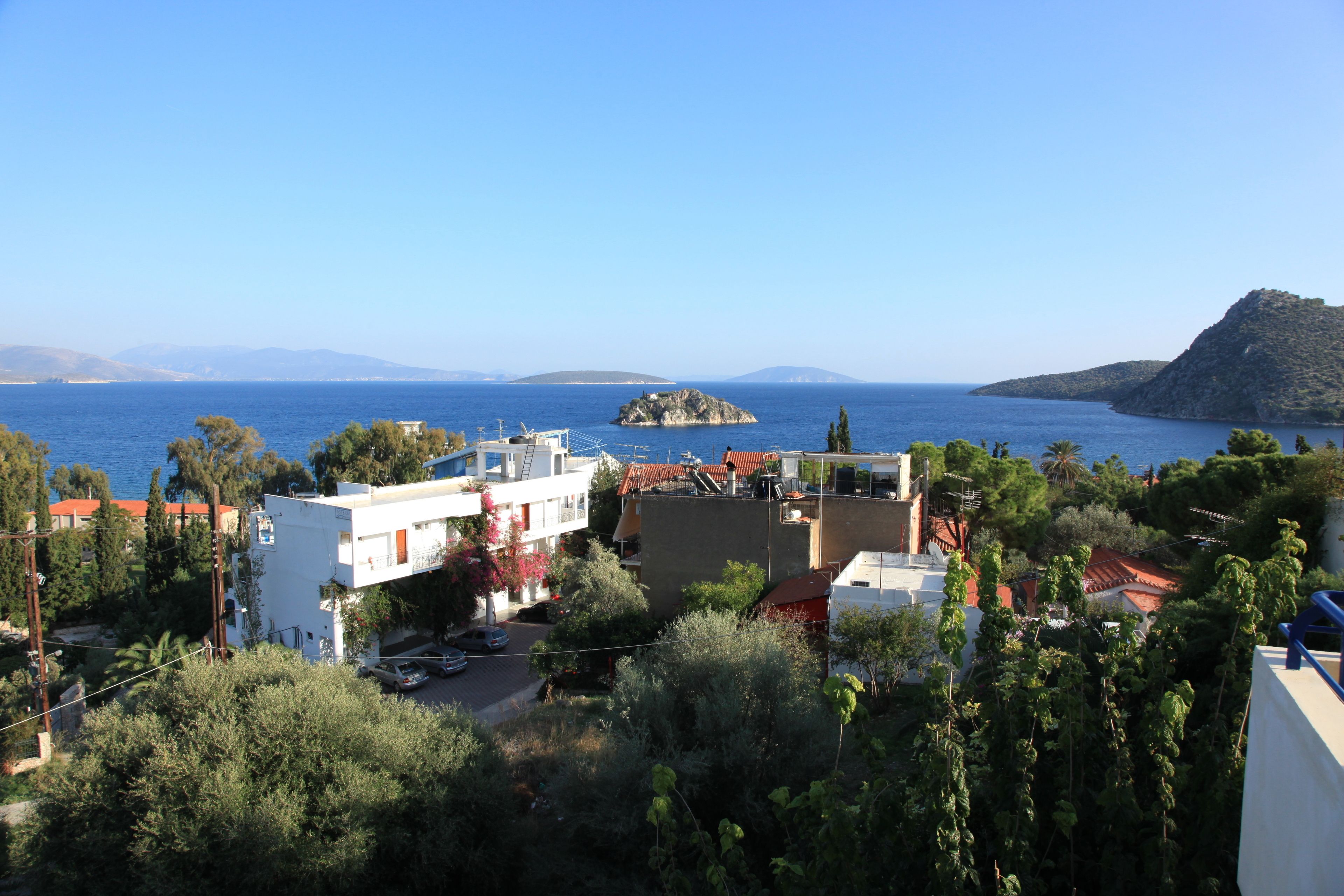 A coastal town with buildings, a clear blue sea, and a distant island.