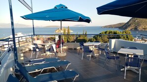 Una terraza con mesas al aire libre, vistas al mar y un paisaje montañoso al fondo.
