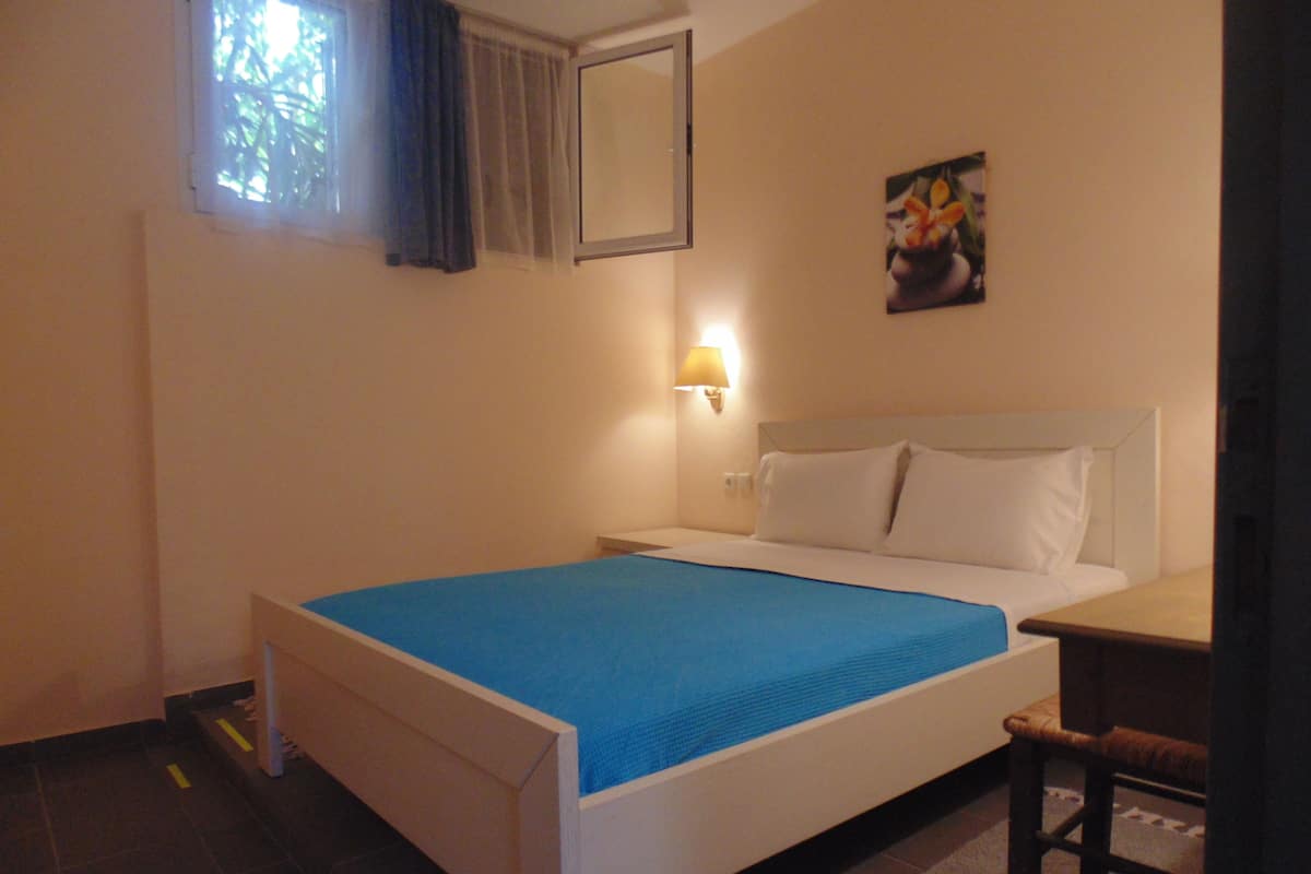 Une chambre à coucher avec un lit, une table de chevet, une lampe, une chaise et un tableau accroché au mur.