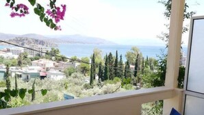Un balcón con una mesa y dos sillas, con vista a un paisaje costero con edificios y árboles.
