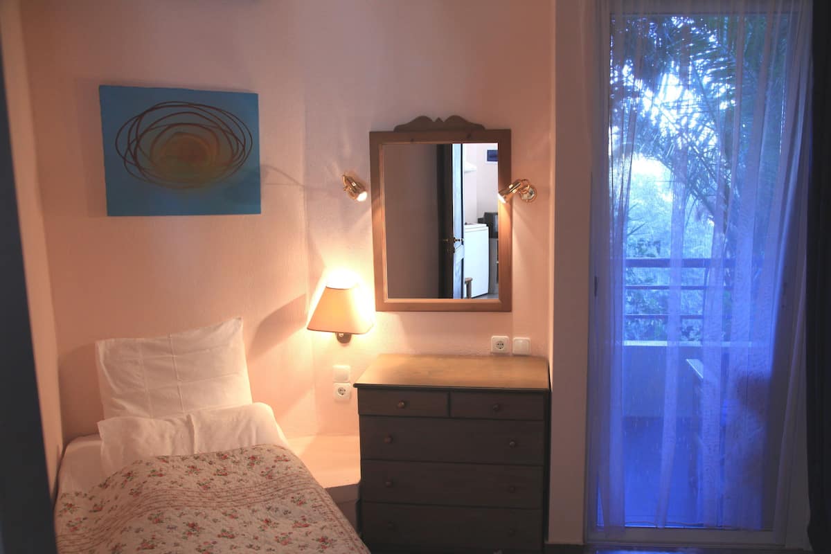 Une chambre à coucher comprenant un lit, une commode, une table de chevet, une lampe, un miroir et une fenêtre avec des rideaux.